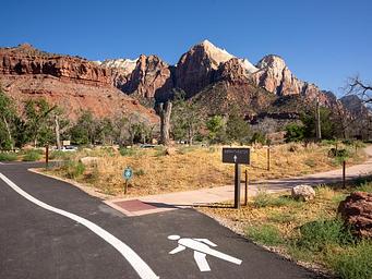 Pedestrian path winding through the campground with sheer, dramatic sandstone cliffs of Zion Canyon rising in the background.