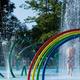 Close-up photo of the campground splash pad/water play area with rainbow arches and fountains — clearly an on-site pool/play amenity (source: homepage images).