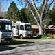 Gravel RV lot with multiple motorhomes and the office/building visible in background; from the park facilities page illustrating the main parking/office area and typical RV pitches.