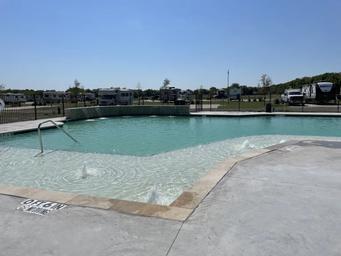 Clear photo of the swimming pool with the RV park visible in the background — highlights on-site recreational amenity. Shown on the property homepage/accommodations content.