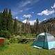 A bright blue-green tent with Slough Creek and woods behind