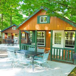 Shows rustic cabins with outdoor patio furniture set on concrete pads surrounded by trees — useful cabin accommodation shot from the campground 'ways to stay' images.
