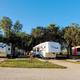 Wide panoramic shot of multiple RV sites and paved pads with trees and gravel road — clear overall overview of the park layout (from the property home page hero).