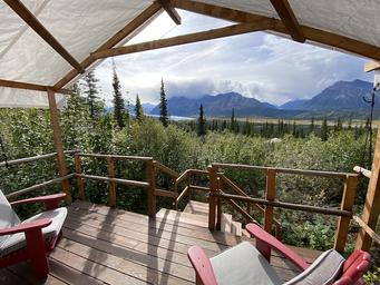 Deck-level daytime view from a tent showing Adirondack chairs and expansive mountain valley scenery — demonstrates guest viewpoint, private deck and the landscape setting guests experience.