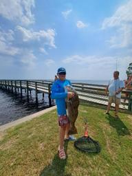 Daytime pier/shoreline photo showing a catch and the pier in the background with grassy shoreline — useful to illustrate on-site waterfront recreation and pier access.  