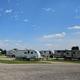 Multiple RVs parked in a camping area under a partly cloudy sky, with a grassy foreground and trees in the background.