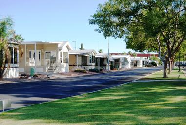 Ground-level street shot showing manufactured homes/RV sites, paved roads and grassy strips — clear view of typical on-site accommodations and landscaping (matches site ‘SR-Street-Shot-a’).