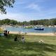 Wide view of the swimming pond with inflatables and sandy beach, grassy seating area and campers in the background — useful shot of the main on-site amenity shown on the homepage.