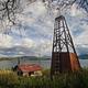 View of a wood cabin and windmill in a grassy field with a lake and mountains in the background.