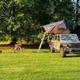 Olive green Jeep with rooftop tent set up on a grassy campsite.