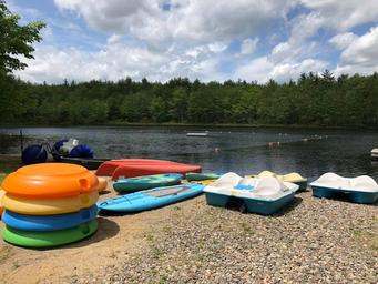 Shoreline image showing paddleboats, kayaks and a small beach area by a lake — represents waterfront recreation available at the campground (appears in site image gallery/assets).