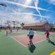 Active recreational area showing pickleball/tennis courts with residents playing and surrounding buildings — demonstrates on-site amenities and community activity (matches site’s community images).