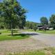 Wide daytime photo showing gravel pads, picnic tables and a fifth-wheel setup with distant tree-lined hills — clear representation of site layout and amenities from the gallery page.