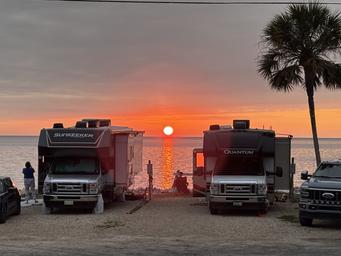 Framed sunset between two RVs looking directly at the water — strong, attractive campsite photo from the property gallery useful for listing.