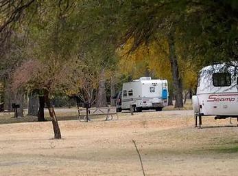 Two travel trailers in campsite with trees lining the sites and roadway
