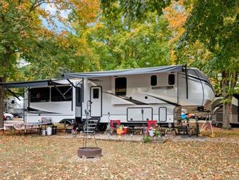 RV site pictured with a large fifth-wheel, fire ring and seasonal foliage — good example of typical RV camping spaces on property (‘ways to stay’ image).