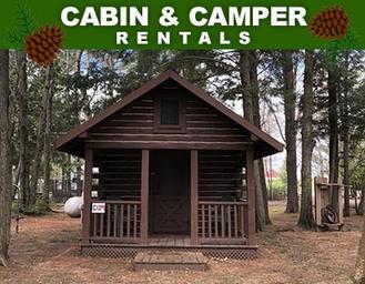 Front view of a rustic cabin among trees labeled 'CABIN & CAMPER RENTALS' on the site — shows lodging option available at Pine Grove.