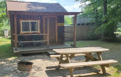 Small cabin with picnic table, fire ring and yard area — clear campsite/cabin setting for guests (source: Rental Rates & Info page).