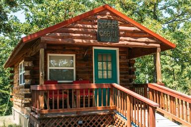 Exterior photo of a rustic cabin (Copper Cabin) on the property — shows cabin frontage, porch, and setting; originates from the site’s gallery and labeled as an on-site cabin.
