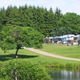 Wide view across a pond to grassy campground area with RVs and hookups visible — useful scenic/site photo (homepage image).