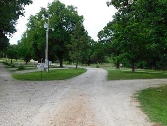 Overview of campground road/drive lanes and RV sites — shows gravel roads, site signage and mature trees, useful for displaying the park layout and RV pitch style (from the gallery).