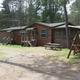 Log cabin with a screened porch, picnic table, and swing set; parked vehicle.