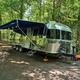 Airstream RV on a gravel site with awning and hookups visible in a wooded site — illustrates RV pitching options and site appearance.