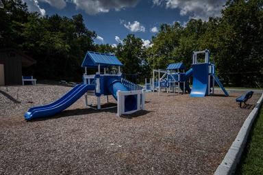 Playground equipment on gravel with trees in background — shows the campground’s play area/amenities (gallery image on main site).