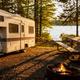 Clear on-site campsite view showing an RV parked beside a picnic table and lakeside firepit surrounded by trees — suitable to represent RV sites/campsites. Source page: homepage large hero image crop.