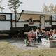 Wide view of an RV campsite with picnic table, firepit and family gathered — useful depiction of a typical full-hookup RV site.