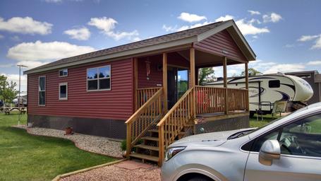 Exterior of a covered-porch cabin on-site showing cabin style, deck and adjacent RV — good for rental accommodation listing (rental unit page).