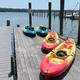 Kayaks docked on a wooden pier beside a calm lake, with blue sky and distant shoreline.
