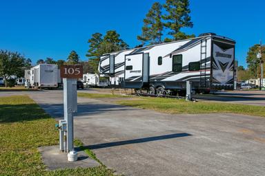 Close view of an individual concrete RV pad with utility pedestal (site marker 105) and multiple RVs in the background — good detail of site size and hookups (from rates/gallery pages).
