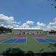 Wide photo showing painted outdoor courts with a large building (likely clubhouse/rec hall) behind them — good overview of on-site recreational facilities; image is hosted on the property site page.