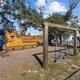 Outdoor playground with a pirate ship play structure, blue spiral slide, and wooden swing set on gravel under oak trees.