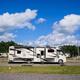 Ground-level view of a single RV on a designated gravel site with utilities visible and surrounding sites in background — good detail of a typical RV pitch.