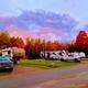 Row of RVs parked at designated concrete pads with hookups and road — good overview of RV pitches and site layout. Image appears on the Home page (fall-pic) showing campground RV sites.