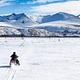 A snowmobile riders crosses a big meadow with mountains in the distance.