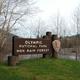 A large brown National Park sign that reads "OLYMPIC NATIONAL PARK - HOH RAINFOREST." The Hoh River can be seen flowing past in the background.