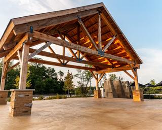 Open timber pavilion/covered outdoor structure on paved area — shows a campground facility/amenity space useful for events and guest gathering.