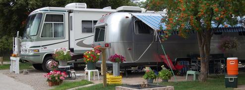 Close view of two RVs on a site with awning, potted plants and site utilities visible — useful for showing site detail and campsite amenities (source: homepage/news images).