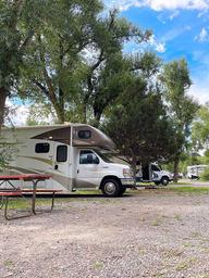 RV campsite row with motorhome, picnic table and mature trees — clear representation of the RV camping area and site setup (from reservation/tent camping page).