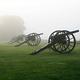 Four civil war cannons along a green foggy field.
