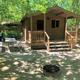 Photograph of a small cabin with porch, picnic table and grill in a wooded setting — depicts the campground’s cabin accommodations (used on the site’s main page). Useful for cabin listing.