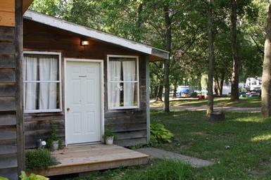 Cabin in a wooded setting with RVs visible in the background — shows lodging/campsite units and site layout from the Campsite page.