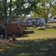 Exterior daytime photo showing campground grounds with grassy lawn, trees, picnic tables, decks and multiple RVs/trailers — clear on-property scene used on the Backyard Campground homepage (site image URL and page context match). Good overall view of campsites and amenities.