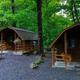 Close view of two small log cabins with gravel pads and porch seating set in trees — useful to illustrate cabin accommodations on the property (image shown on the campground page).