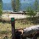 Site marker eleven in foreground; picnic table in a flat gravel area with bushes encircled with log barrier, river valley and conifer covered hills in background.