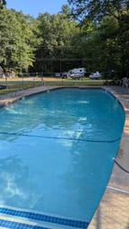 Empty swimming pool in an outdoor setting with a fence, chairs, and trees in the background.