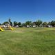 Daytime wide shot showing grassy common area with playground and a row of RVs/cabins in the background — useful overview of campsites and family amenities. Image appears as a background/photo on the site’s home page, indicating it depicts the property.